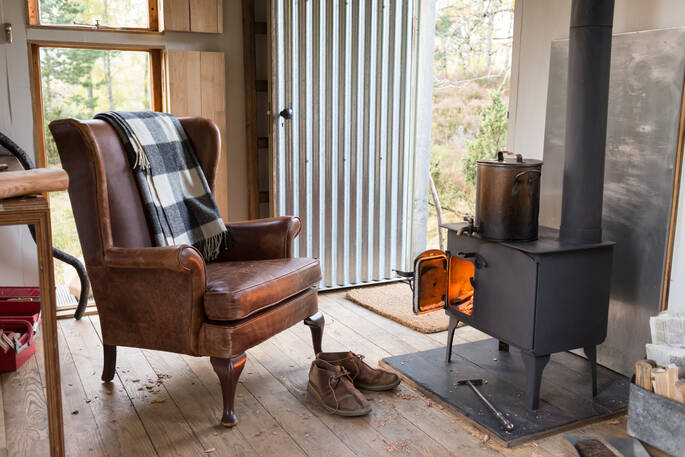 Sit by the wood-burner inside The Bothy Project at Inshriach House in Highland 