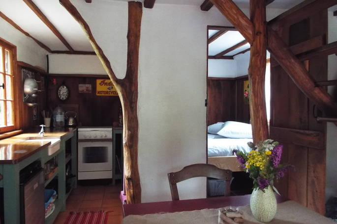 A view of three rooms in one, on the left is the fully-equipped kitchen, with oven and cooker, In the middle is a nice dining area with comfortable chair and beautiful flowers in a vase, on the right you can see the cosy bedroom at Fisherman's cabin in France