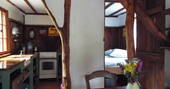 A view of three rooms in one, on the left is the fully-equipped kitchen, with oven and cooker, In the middle is a nice dining area with comfortable chair and beautiful flowers in a vase, on the right you can see the cosy bedroom at Fisherman's cabin in France