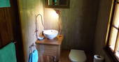 Bathroom at Fisherman's Cabin, with sink and toilet and wooden panels on the wall, and teal towels, Dordogne, France