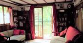 Te cosy living room of the Fisherman's cabin in the Dordogne in France. Cute patterened fabrics cover the comfortable sofas, along with cherry pink pillows and throws. Through the window the gorgeous view on the river and trees can be seen through the window