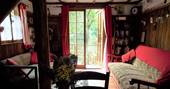 The sitting room at Fisherman's cabin with a bookcase next to the comfortable sofa and glass doors that open to a view of the beautiful tranquil lake in the Dordogne in France