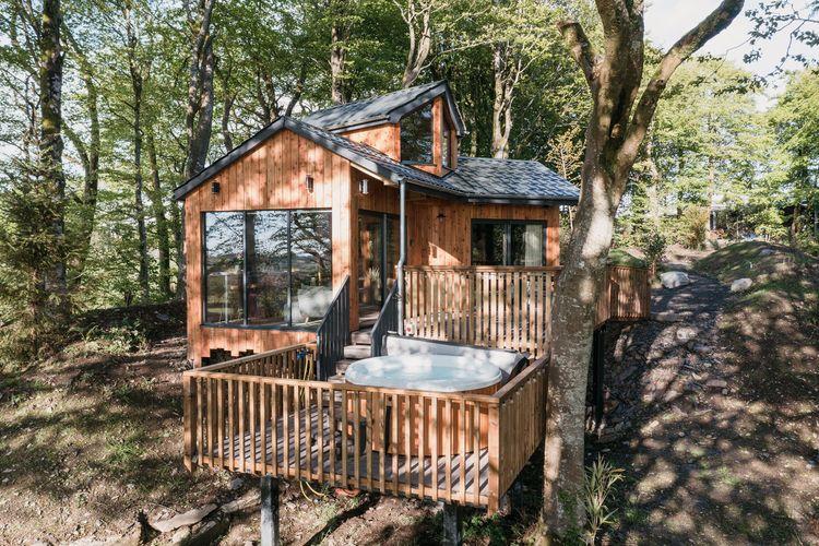 A large treehouse in the woods with a hot tub on the front deck