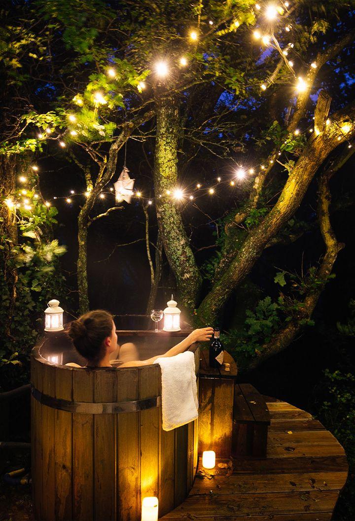 Person in hot tub with woodland, fairy lights and candles 