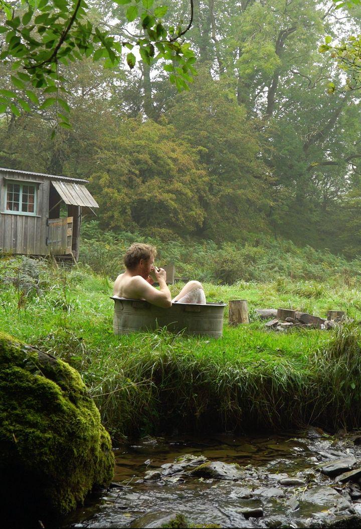 Person sitting in rustic tub on riverside