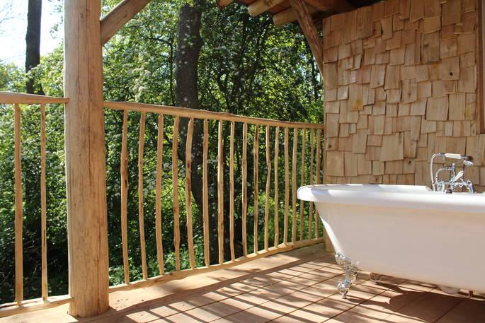 Treehouse decking with outdoor bath and view of woodland 