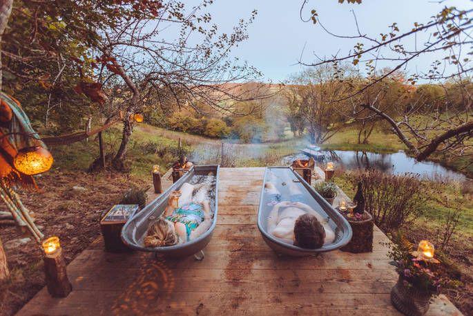 Two people in outdoor baths on decking overlooking river