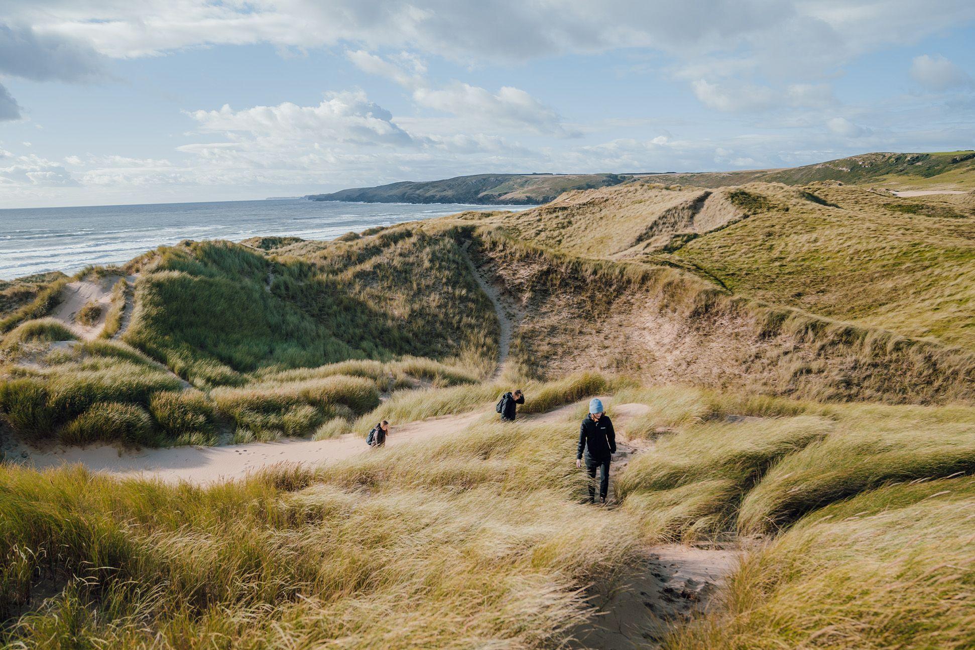 People walking through sand dunes wearing jumpers and hats 