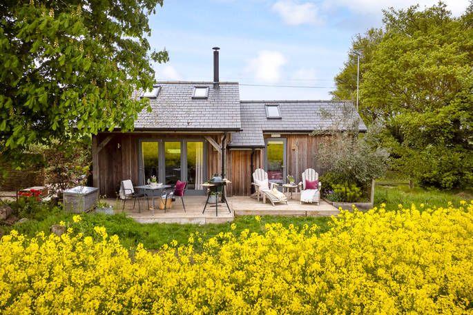 Hare Field Cabin  outside with yellow flowers, BBQ, and outdoor seating on the decking