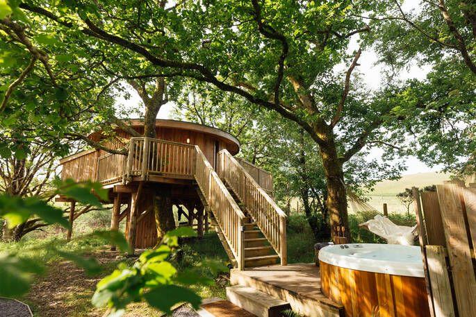 Ty’r Derw Treehouse exterior with outdoor hot tub under trees 
