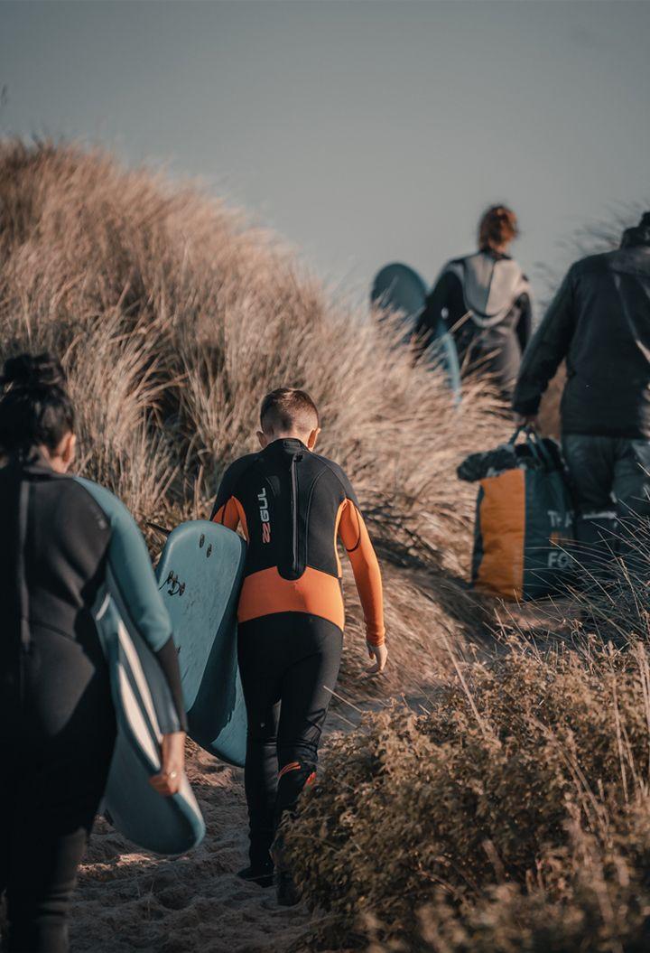 Family walking over sand dunes with surf boards