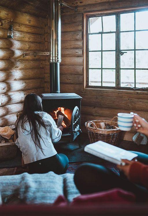 A person reading and a person lighting a wood burner 