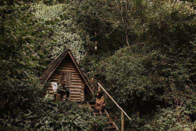 A cabin in the woods with two people outside 