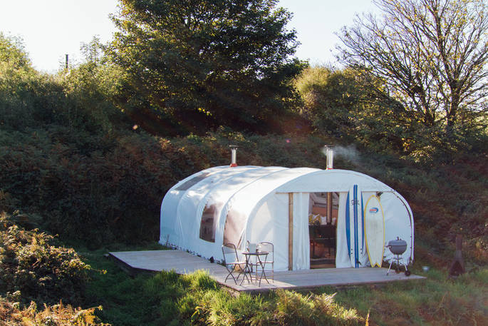 Exterior of Steren pod that has wooden decking with seating area and BBQ surrounded by trees at Ekopod