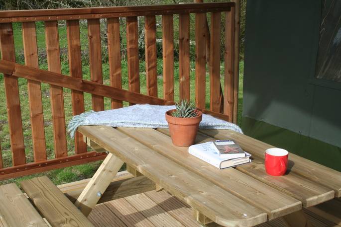 Relaxing wooden bench area outside of the Safari tent with blanket and books