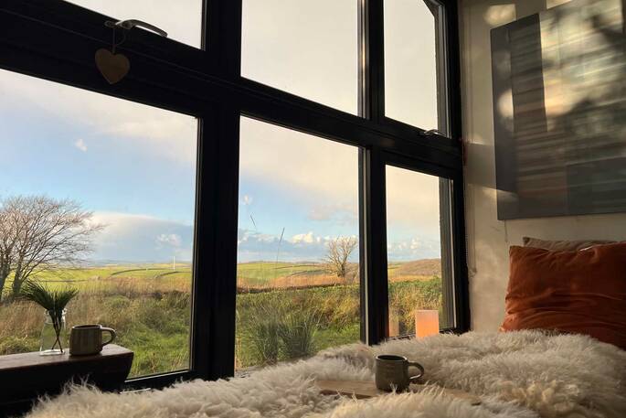 A comfy double hammock in the sun, overlooking the beautiful calm countryside with yellow and green fields, under a blue sky at Quiet of Stars in Cornwall