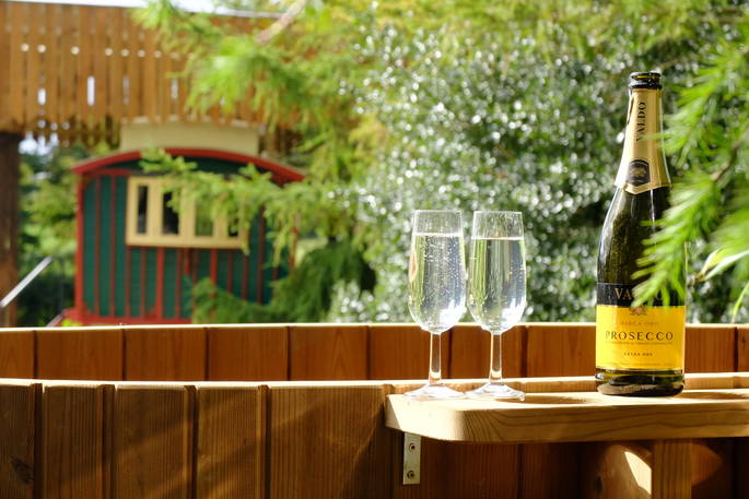 Two glasses of bubbly prosecco sit side by side on the edge of the wood fired hot tub at Sangers Showman's Wagon, Cornwall