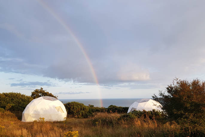 Two of the Geodomes with sea views and a rainbow at Wilderme in Cornwall