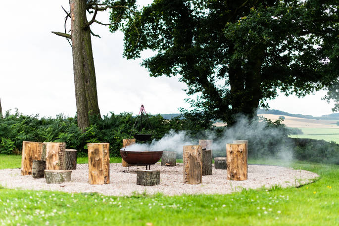 Sit with friends around the fire pit, with views of rolling fields, at The Bothy at High Barn in Cumbria