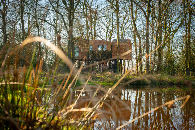 Exterior of Faraway Treehouse infront of the river hidden in the woods in Cumbria