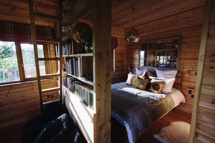 The comfortable and cosy double bed, and mezzanine accessed by a ladder inside Netherby Treehouse in Cumbria