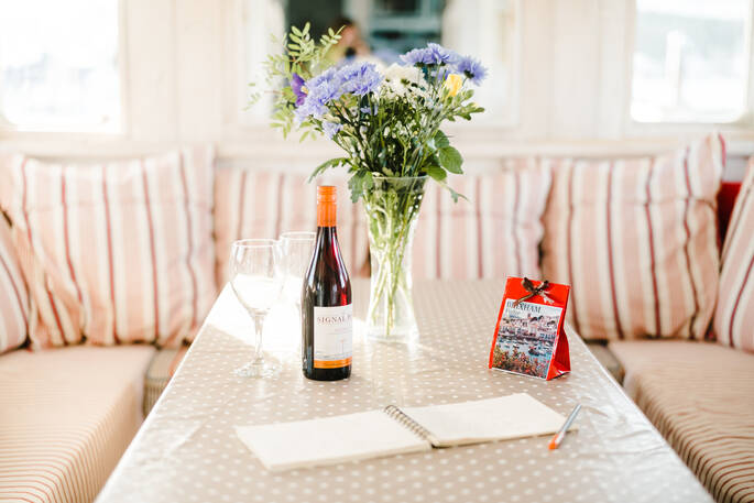 The comfortable dining area aboard boat Faithful in Devon decorated with a vase with purple flowers, with a delicious bottle of wine and some excellent local treats to enjoy