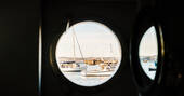 The view through a porthole aboard Faithful ship shows sailing boats in the tranquil picturesque Brixham Marina, Devon