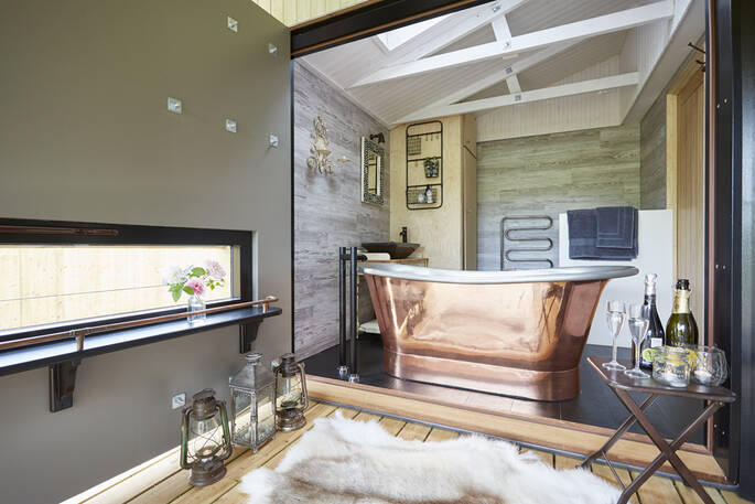 Enjoy romantic baths in the giant copper tub for two in the en suite bathroom of Brownscombe Cabin. Champagne bottle and glasses sit on a table next to bath