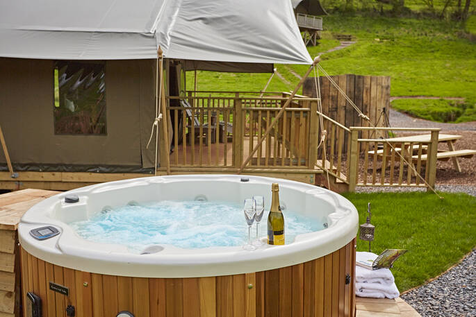 Two glasses of fizz sit by the private hot tub of Yealm safari tent at Brownscombe in Devon
