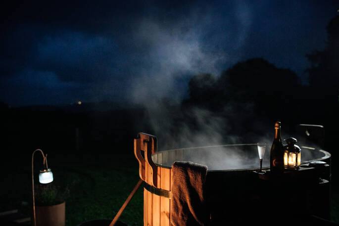 The wood-fired hot tub at night at Little Links yurt, with a bottle of wine sitting on the edge