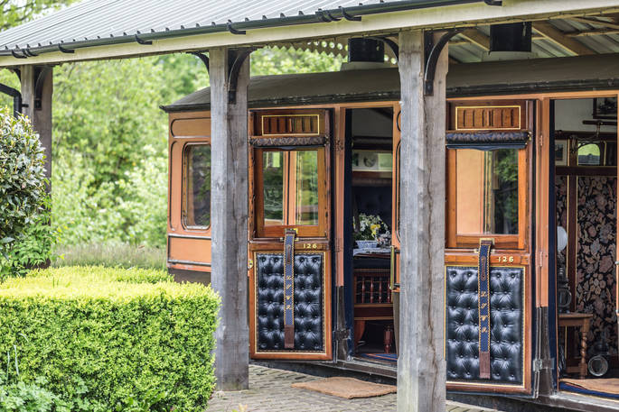 Beautiful wooden vintage train carriage under roofing. Doors with leather panelling open to show the decorated interior at Camping Coach, Dorset