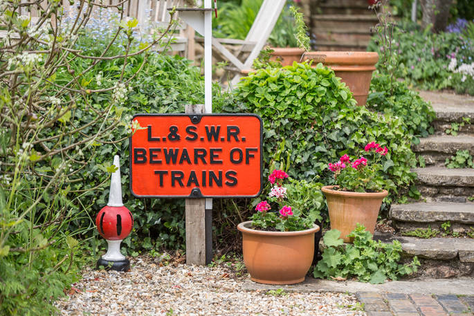 Railway sign at Camping Coach, text reads "L.& S.W.R. Beware of Trains", two flower pots are standing next to it, at Camping Coach, Dorset