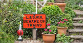 Railway sign at Camping Coach, text reads "L.& S.W.R. Beware of Trains", two flower pots are standing next to it, at Camping Coach, Dorset