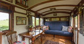 Interior of Camping Coach, with comfortable blue sofa bed with colourful pillows, and beautiful antique dining table and chairs, Dorset