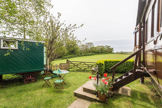 The garden at Camping Coach with green garden table and chairs, the living van and camping coach on either side, looking out onto the peaceful rolling downs of Dorset