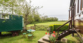 The garden at Camping Coach with green garden table and chairs, the living van and camping coach on either side, looking out onto the peaceful rolling downs of Dorset