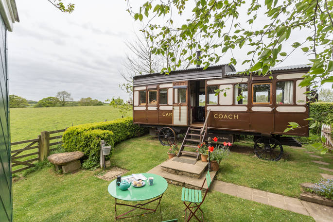 Quirky train carriage Camping Coach in Dorset, with steps leading down to the grassy garden with green garden table and chair.