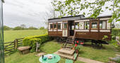 Quirky train carriage Camping Coach in Dorset, with steps leading down to the grassy garden with green garden table and chair.