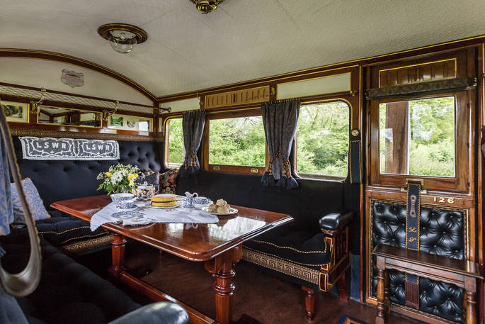 Stunning luxurious interior of vintage train carriage with comfortable benches around a beautiful antique wooden table with a delicious Victoria Sponge cake on it, at Camping Coach, Dorset