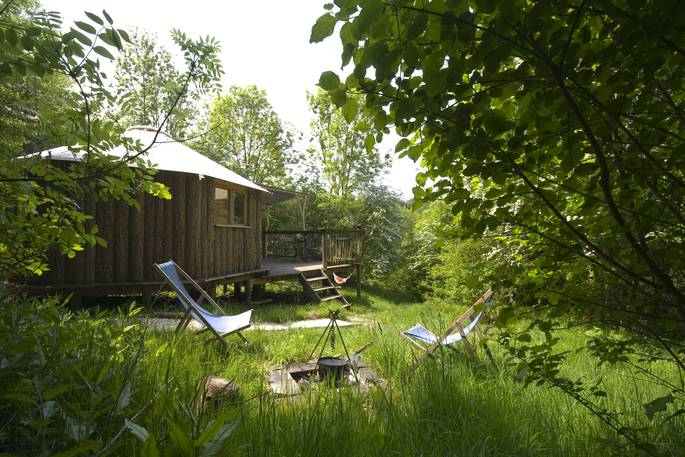 Gold Rush Cabin though the trees at Westley Farm in Gloucestershire with fire pit and outdoor seating