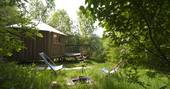 Gold Rush Cabin though the trees at Westley Farm in Gloucestershire with fire pit and outdoor seating