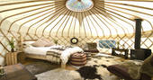 Interior of Yurt Reynolds with double bed and wood-burner at Westley Farm in Gloucestershire 