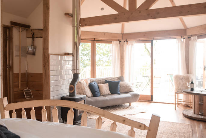 Look across the large living space with comfy sofa, log burner and table to sit at, at Venn Treehouse in Herefordshire