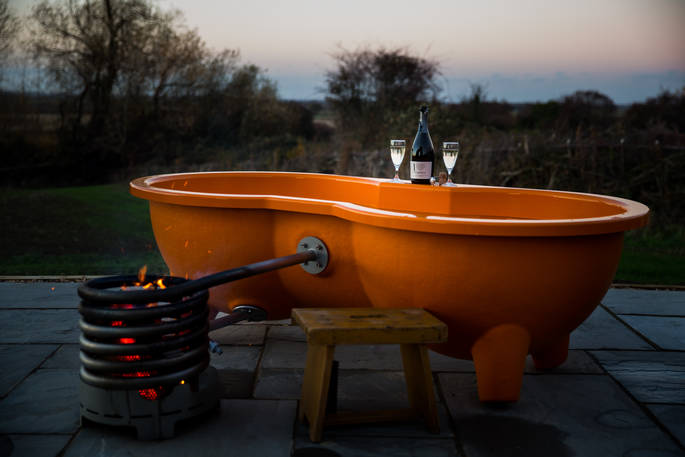 Relax in the outdoor hot tub with a glass of bubbly outside your shepherd’s hut at Tin and Wood