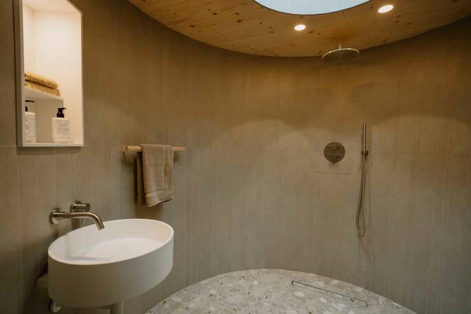 Round bathroom with a rainfall shower, sink and flushing toilet