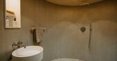 Round bathroom with a rainfall shower, sink and flushing toilet