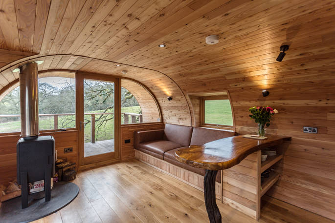 Curved interior walls of Cheriton Treehouse living space with woodburner and fold out sofa bed next to doorway out to elevated deck
