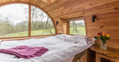 Handcrafted double bed surrounded by windows with views of the surrounding greenery out for Cheriton Treehouse in Somerset