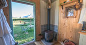Inside the cosy and rustic Jesters Shepherd's Hut at Hill Farm, with log burner and fluffy robes hanging on the wall