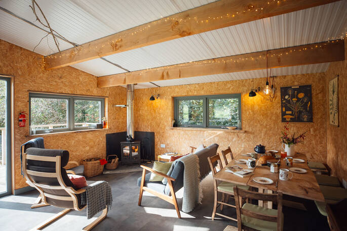 Communal living area with dining table with seating for eight, sofas and wood burner